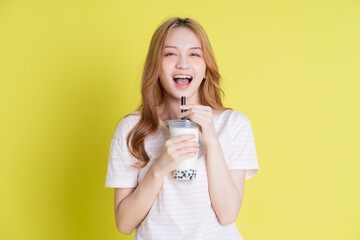 Image of young Asian girl drinking milk tea on yellow background - Powered by Adobe