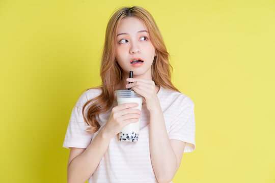 Image of young Asian girl drinking milk tea on yellow background