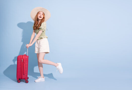 Full length image of young Asian girl with suitcase on blue background, travel concept