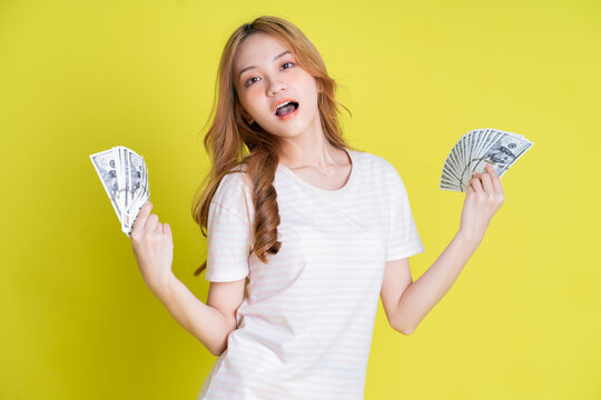 Image of young Asian girl holding money on yellow background