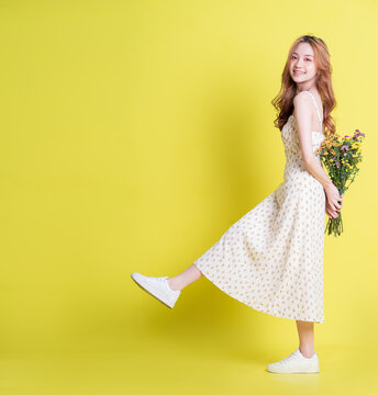 Image of young Asian woman holding flowers on yellow background