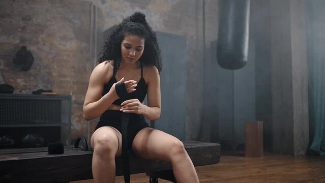 Woman with kinky hair sits on pommel horse wrapping hands