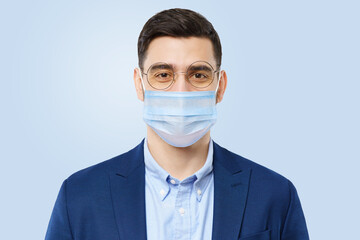 Young casual man wearing medical mask stands isolated on blue background