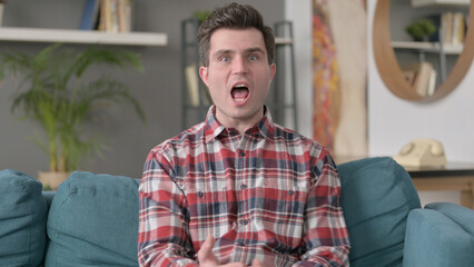 Portrait of Man Getting Angry on Video Call, Sitting on Sofa 