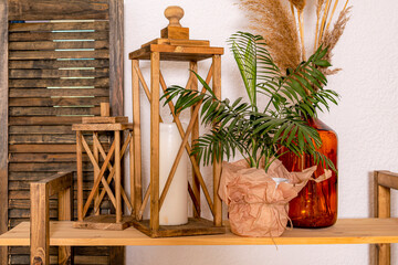 Decorated room: wooden shelf with lanterns with candles, vase with flower against background of wall and a screen. Cozy furnished living room.