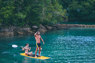 Summer holidays vacation travel. SUP Stand up paddle board. Young woman and man sailing together on beautiful calm lagoon.