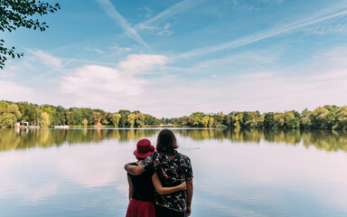 Obraz premium verliebtes Paar stehend von hinten an einem See mit Blick auf das Wasser mit Blick in die friedliche Zukunft in Familie