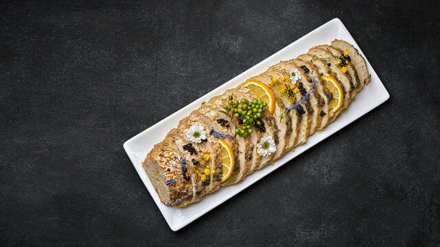 Sliced stuffed fish with lemon, on a plate, on a dark background with space for text