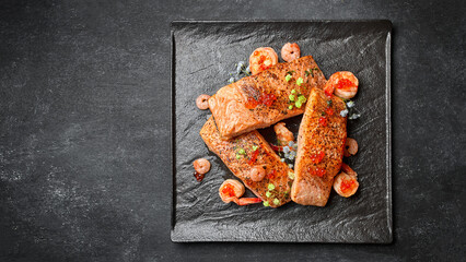 Fried salmon steaks with shrimp and red caviar, on a black plate, on a dark background with space for text
