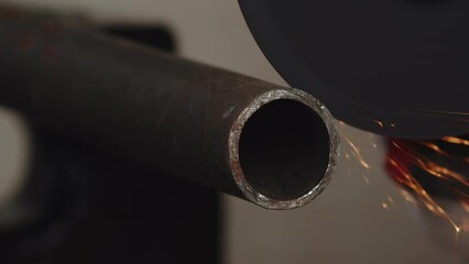 Closeup of metal pipe that is being sawed by an angle grinder with cutting disc, sparks everywhere. Artisan sawing metal pipe using angle grinder