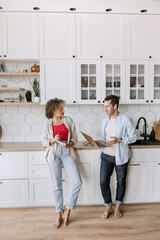  Stylish business partners are working on a project at home in the kitchen, discussing ideas. Happy colleagues studying financial charts, using laptop, talking about new strategy, smiling. business