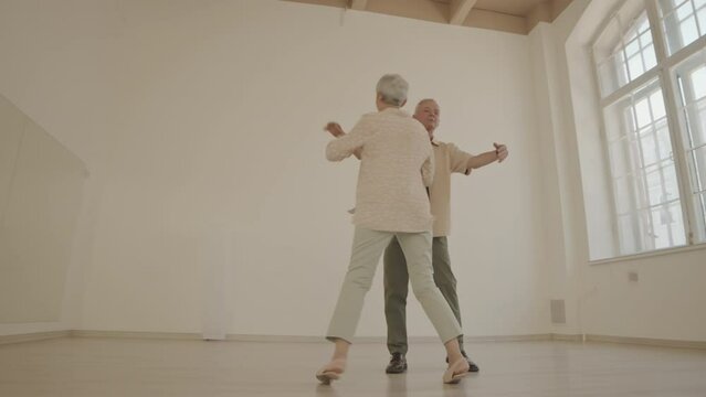 Full length shot of active senior couple ballroom dancing and having fun at bright spacious dance studio