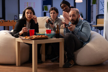 Diverse group of people playing video games on console, using controller on tv at office celebration with drinks and food. Colleagues enjoying after work party with alcoholic beverage and game.