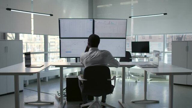 Back view of African-American financial analytics looking at multiple screens with data 