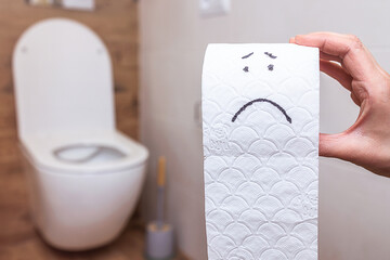 Funny face drawn on a roll of toilet paper on the background of the bathroom