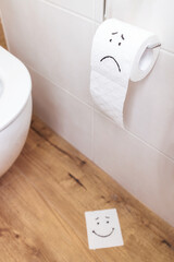 toilet paper with sad face hangs on the wall, paper with funny face on the floor