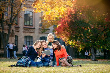 Surfing the net together. Four happy attractive female caucasian students looking at tablet pc and...