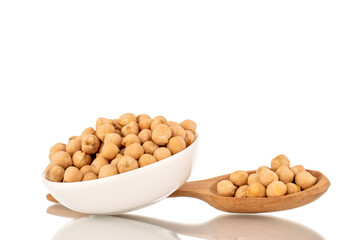 Several uncooked hummus grains in a white ceramic saucer and with a wooden spoon, close-up, isolated on white.