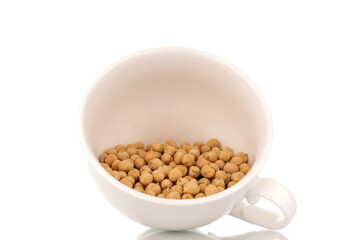Several uncooked hummus grains in a white ceramic cup, close-up, isolated on white.