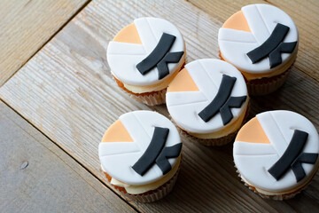 Five little cakes are lying on the wooden background. Cakes in white clothes with black belts. Karate clothes on the cakes