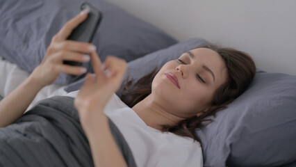 Obraz na płótnie Canvas Woman using Smartphone while Sleeping in Bed