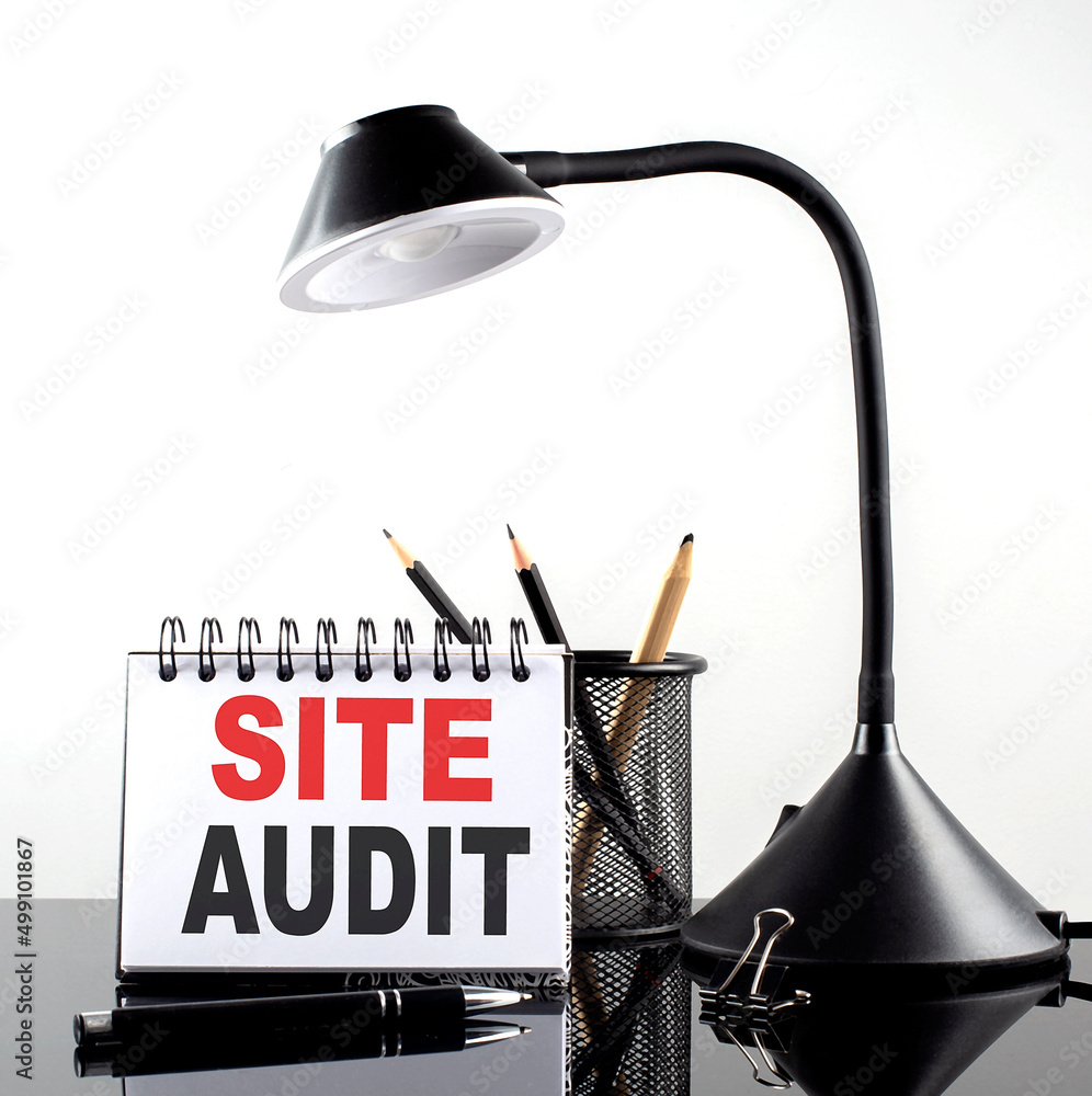Poster site audit text on notebook with pen and table lamp on the black background