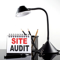 SITE AUDIT text on notebook with pen and table lamp on the black background