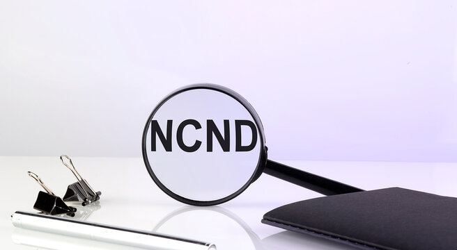 NCND text concept. Magnifier glass with text with notebook and pen,business