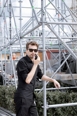 Installation of stage equipment and preparing for a live concert open air. Event manager portrait. Summer music city festival. Man speaks the walkie-talkie.