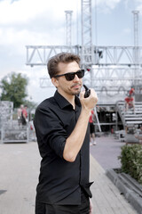Installation of stage equipment and preparing for a live concert open air. Event manager portrait. Summer music city festival. Man speaks the walkie-talkie. - 499102223