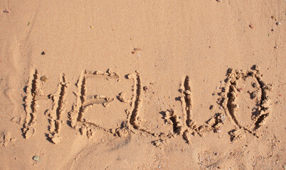 boy draws Hello on the sand by the sea in summer