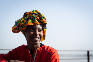 Portrait of a radiant African beauty wearing a red caftan and a colorful headscarf with a...