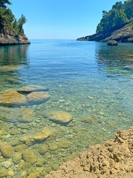 Pebble beach with clear sea water by rocky Mediterranean coast at summer sunny day.