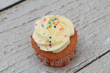 Sweet cake with tutti frutti sprinkles on top on the wooden table white background.