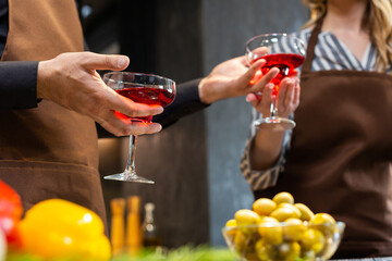 Close-up. Man and woman in the kitchen with glasses of red wine.