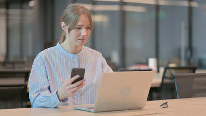 Fototapeta premium Young Woman using Smartphone while using Laptop in Office 