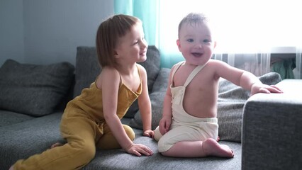Cute toddler kids play hugging together on a gray sofa in the living room, real scandinavian interior, sibling love and relationships, lifestyle