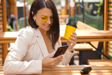 Beautiful brunette lady is sitting in the courtyard of restaurant, drinking coffee, listening to...