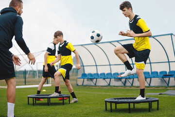 Teenage boy in football training with personal coach. Soccer players improving agility soccer skills. Boy kicking soccer ball standing on fitness trampoline
