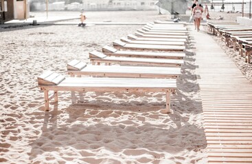 Sun loungers on the beach near the sea. Empty resort. Chaise lounge - beach wooden furniture for...