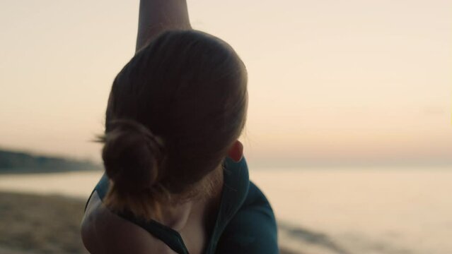 Sporty woman performing utthita trikonasana on beach summer morning close up.