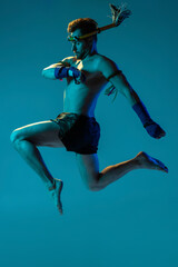 Obraz na płótnie Canvas Dynamic portrait of professional thai boxer practicing isolated on blue studio background. Sport, muay thai, competition, fight club concept