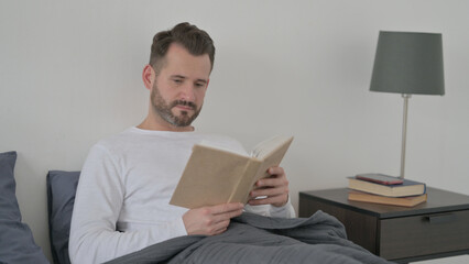 Man Reading Book while Sitting in Bed