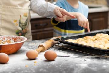 Mom and son try sweet puff pastry lying on parchment on a baking sheet at home in the kitchen. Nearby lies a rolling pin and a bowl. Selective focus. Portrait. Close-up