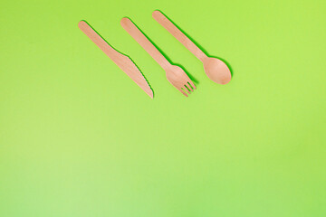 Spoon, fork, knife as cutlery made of natural material on bright green background with copy space. Minimal zero waste concept. Ecological idea for template, design, web banner, restaurant.