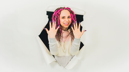 Naklejka premium Young woman showing manicure in hole of white background. Beautiful female with curly hair showing her hands with polish nails in studio.