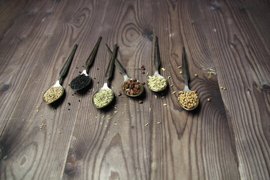 Metal vintage spoons with spice seeds of anis, nigella, ajowan, coriander, rosemary, Sichuan pepper on brown wooden table