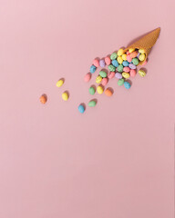 Colorful Easter Eggs fell out of the ice cream cone on pastel pink background with copy space for greeting message. Minimal Easter concept combined with summer vibe.