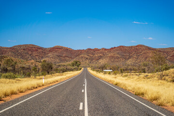 Outback road near Alice Springs with the East Macdonnell Range on the horizon. Northern Territory, Australia.