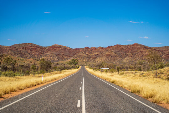 Outback road near Alice Springs with the East Macdonnell Range on the horizon. Northern Territory, Australia.